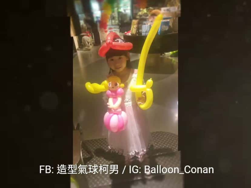 小女孩戴紅色蝴蝶結氣球頭飾，拿著粉紅公主和黃色寶劍造型氣球