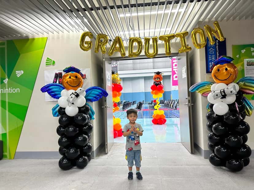 球場入口上方掛著金色 GRADUATION 字母，兩側是戴學士帽、有翅膀的畢業天使氣球柱