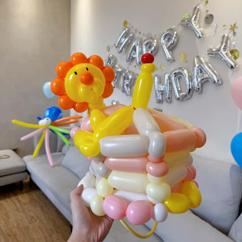 小獅子坐在多層蛋糕上的造型氣球帽，背後是 HAPPY BIRTHDAY 字母
