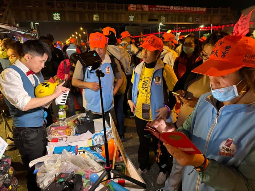 柯男在慈后宮牌樓下的攤位折氣球，戴橘帽的香客圍在桌邊