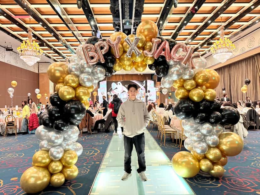 宴會廳場：伸展台上的黑金銀氣球拱門，兩側是圓桌宴席