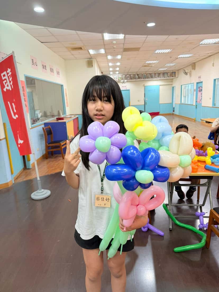 掛名牌的女孩捧著自己做的一大束紫、藍、黃、粉色氣球花
