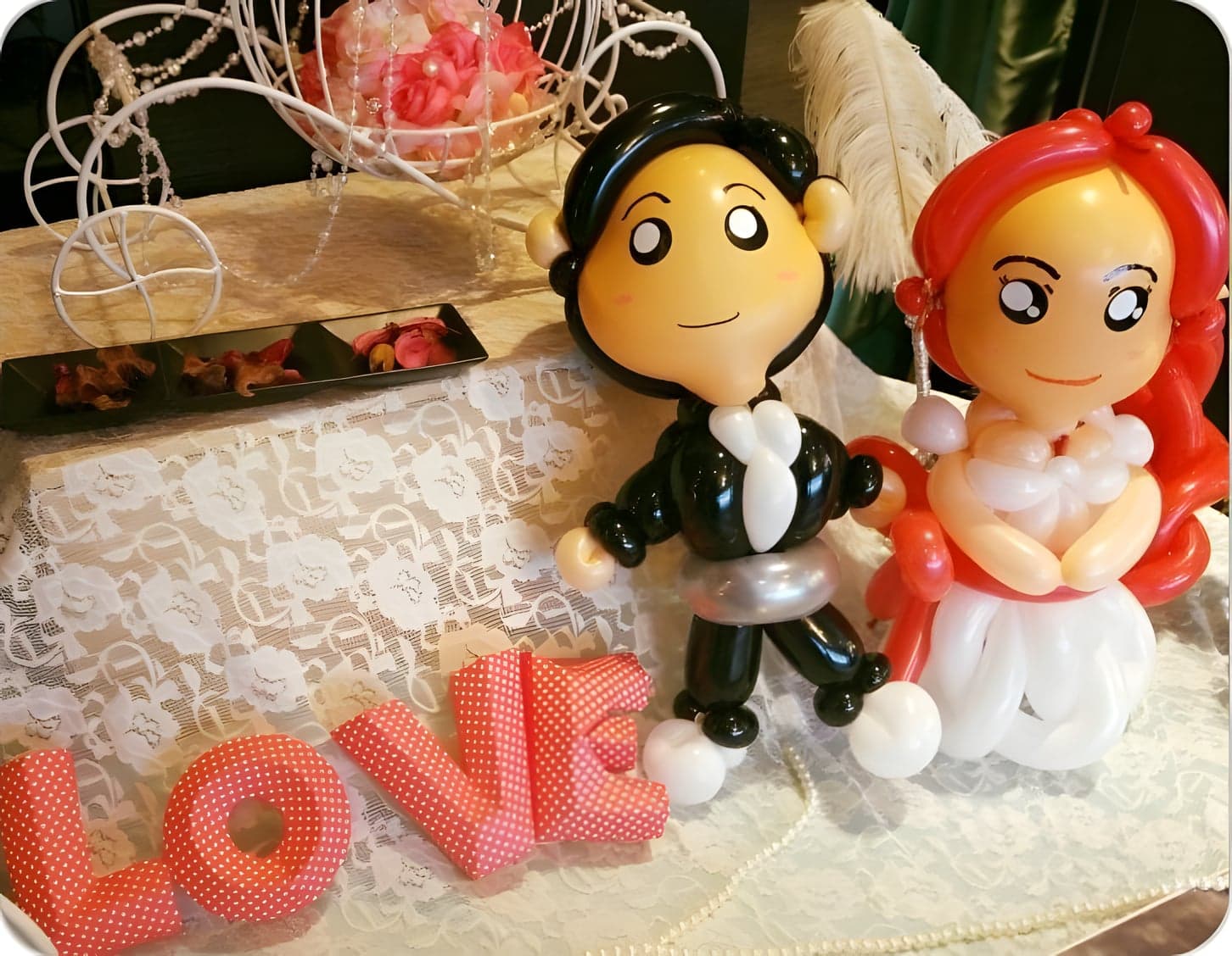 婚禮桌上的新郎新娘氣球人偶，旁邊是紅色 LOVE 字母擺飾