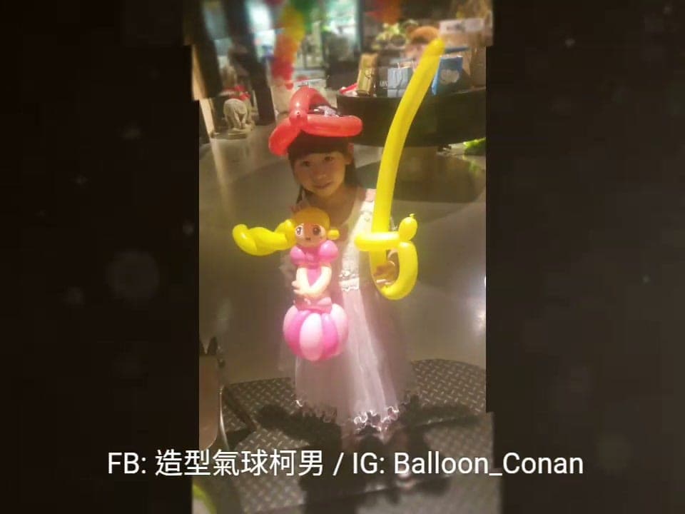 小女孩戴紅色蝴蝶結氣球頭飾，拿著粉紅公主和黃色寶劍造型氣球