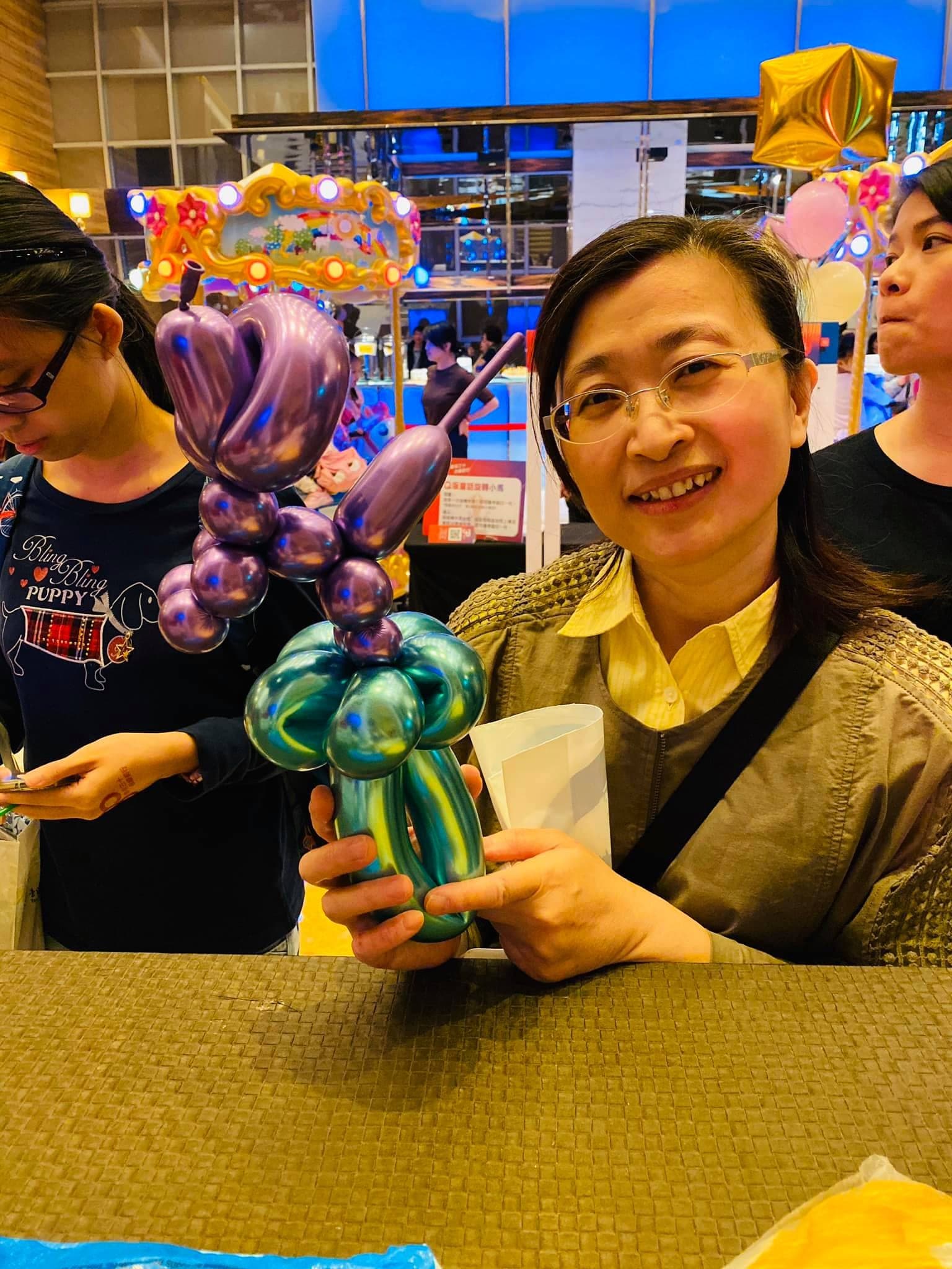 女士拿著紫色與藍綠色金屬氣球做的造型
