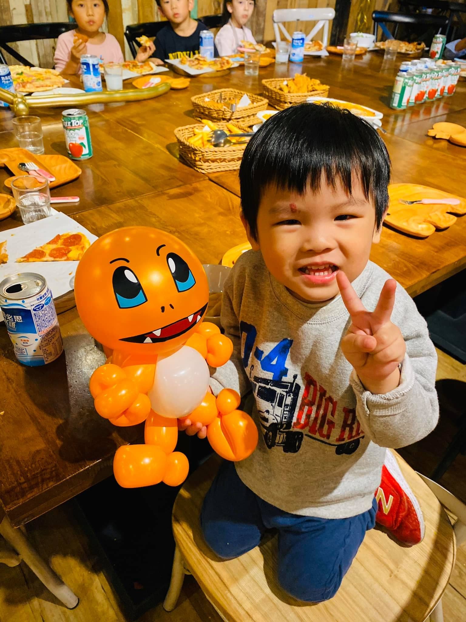 跪在椅子上的男孩比 YA，手扶橘色小火龍造型氣球