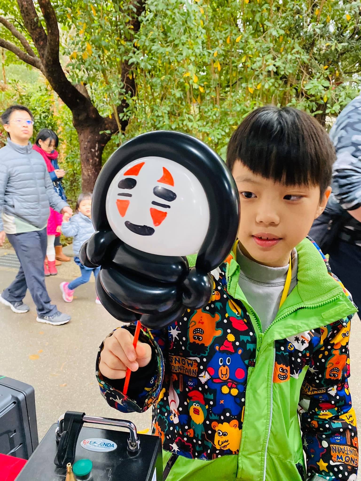 穿彩色外套的男孩舉著無臉男造型氣球手持棒