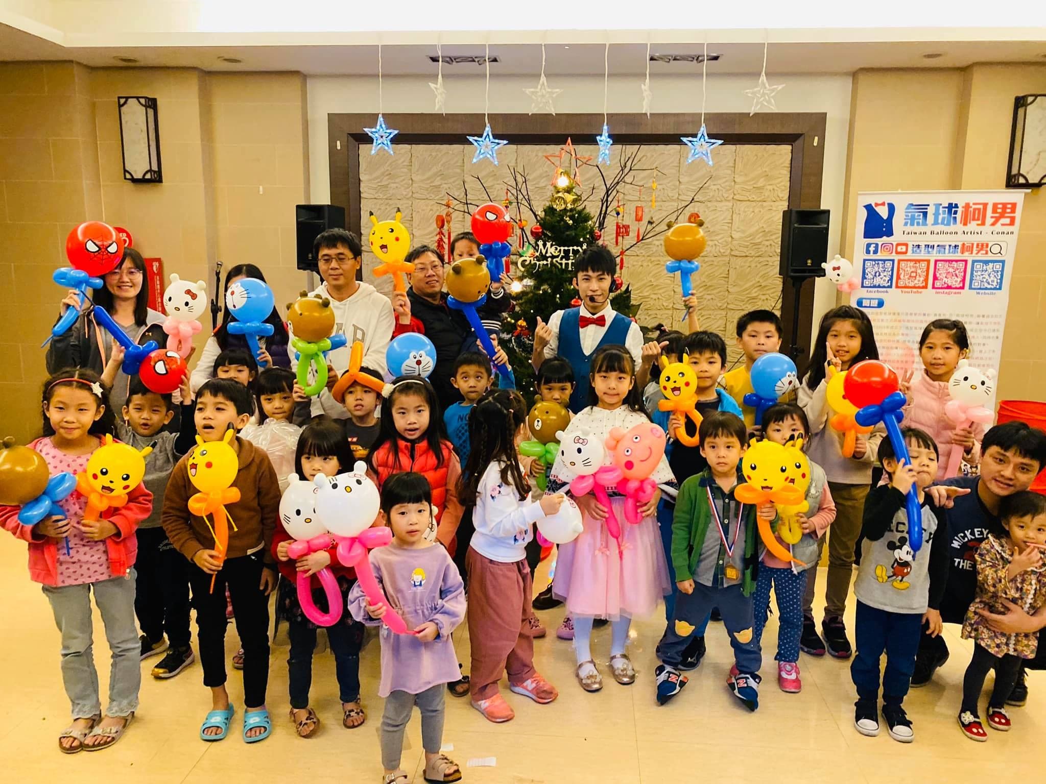 土城社區聖誕樹前的大合照，孩子們舉著皮卡丘、Hello Kitty、哆啦A夢等氣球手持棒