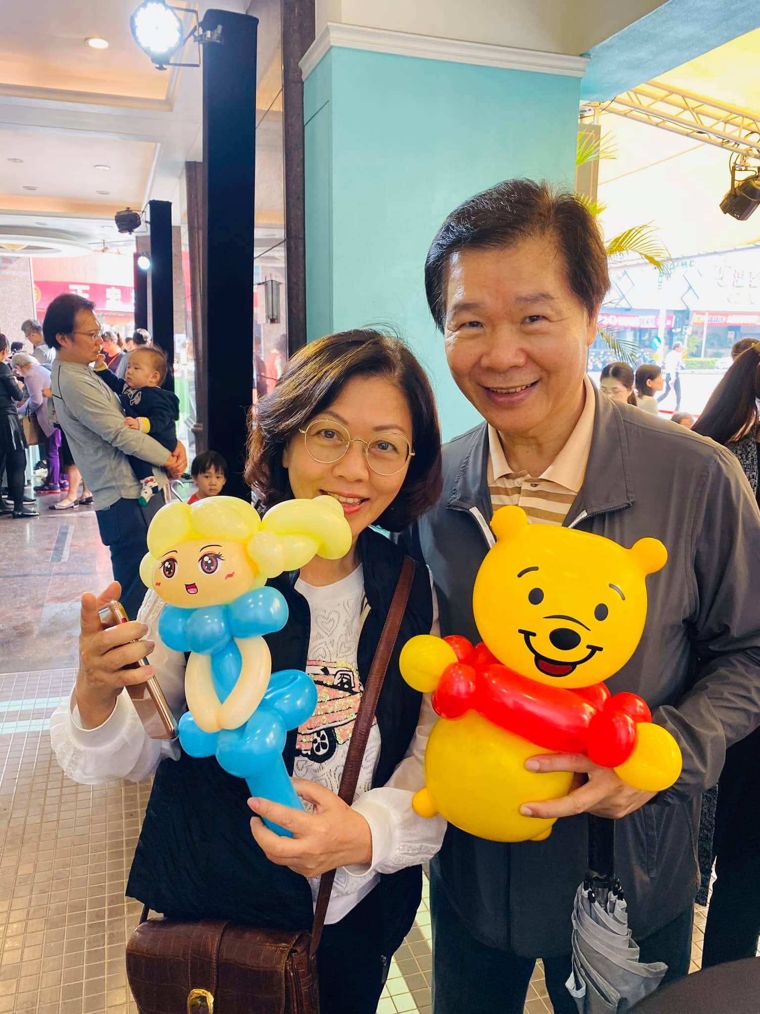 一對夫妻分別拿著金髮藍衣公主和小熊維尼氣球
