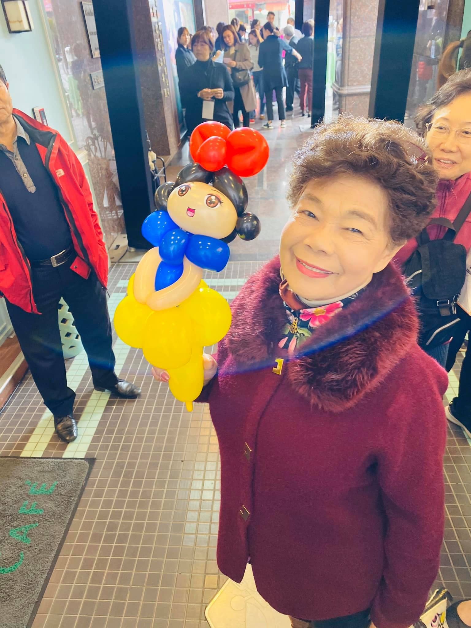 穿酒紅色外套的奶奶開心地拿著白雪公主氣球