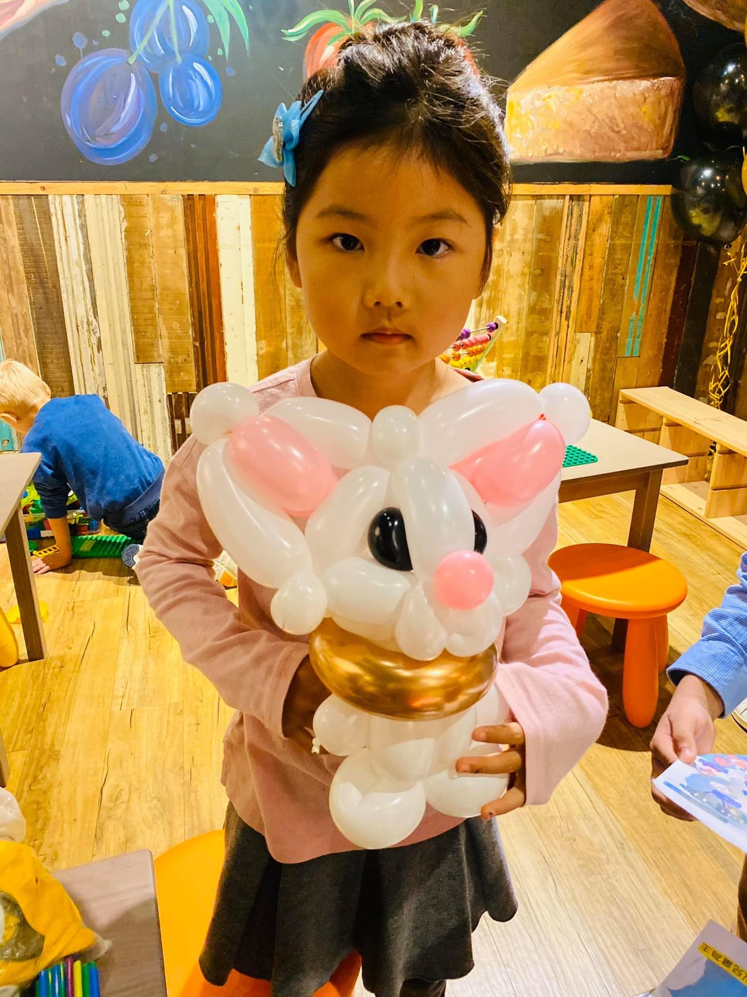 小女孩抱著坐在金色杯子裡的白色兔子造型氣球