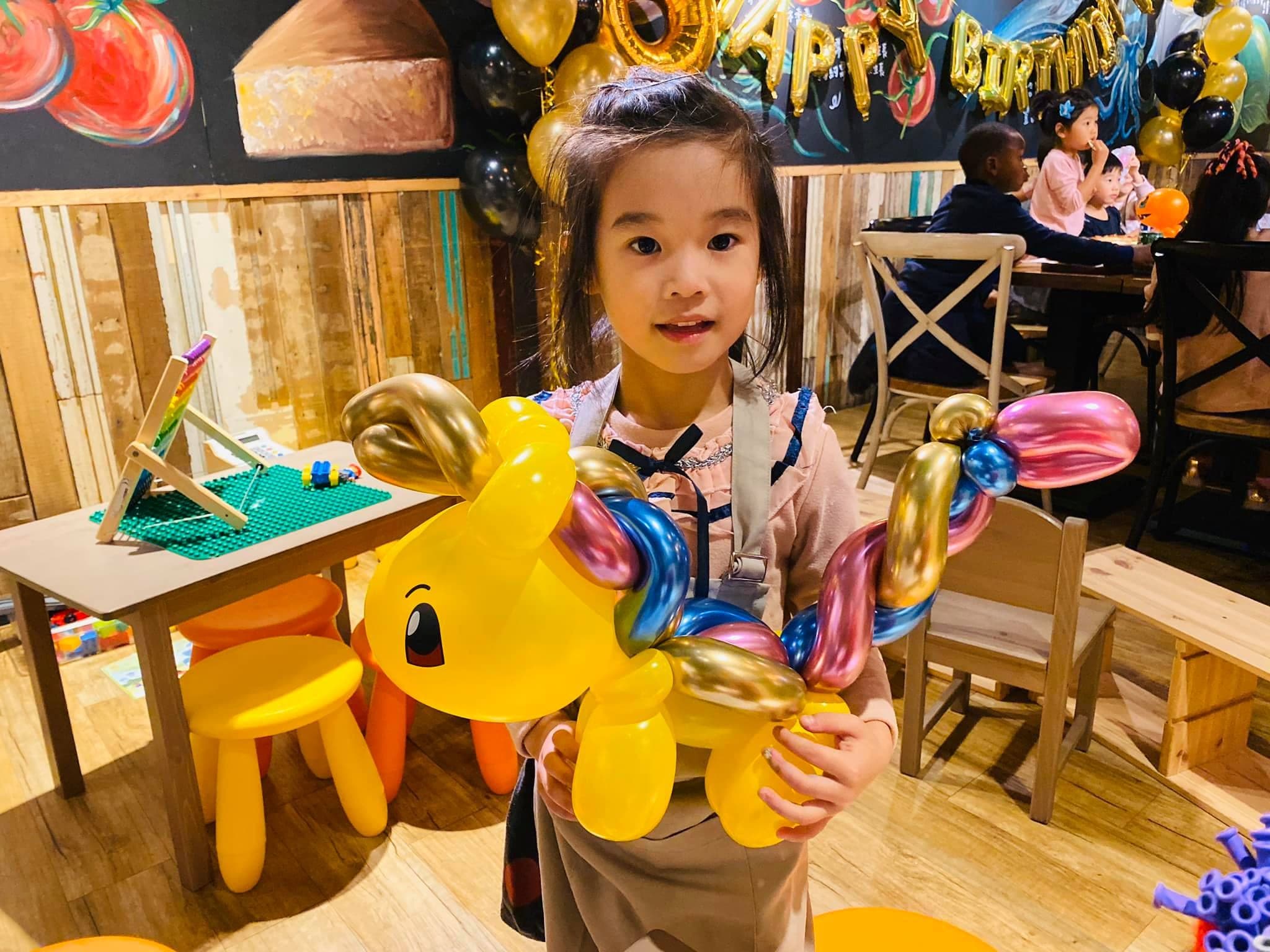 另一位女孩拿著黃色彩虹鬃毛小馬，背景是生日佈置