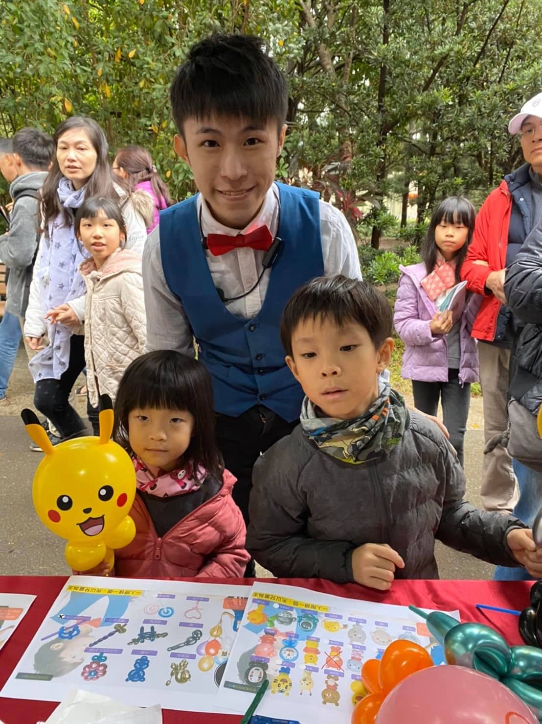 攤位桌前，我站在兩個孩子後方，女孩拿著皮卡丘氣球