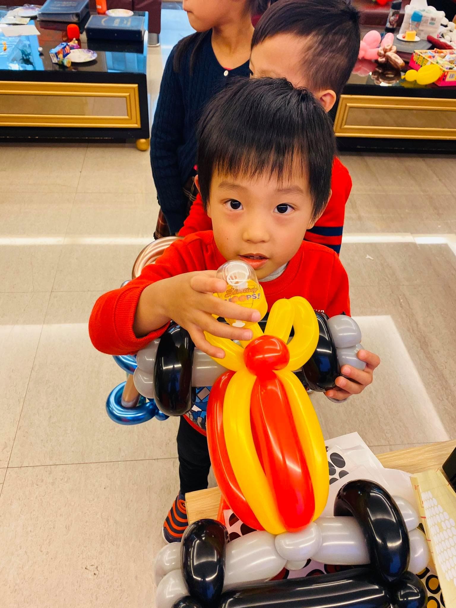 小男孩抱著黑色車輪、紅黃車身的摩托車造型氣球