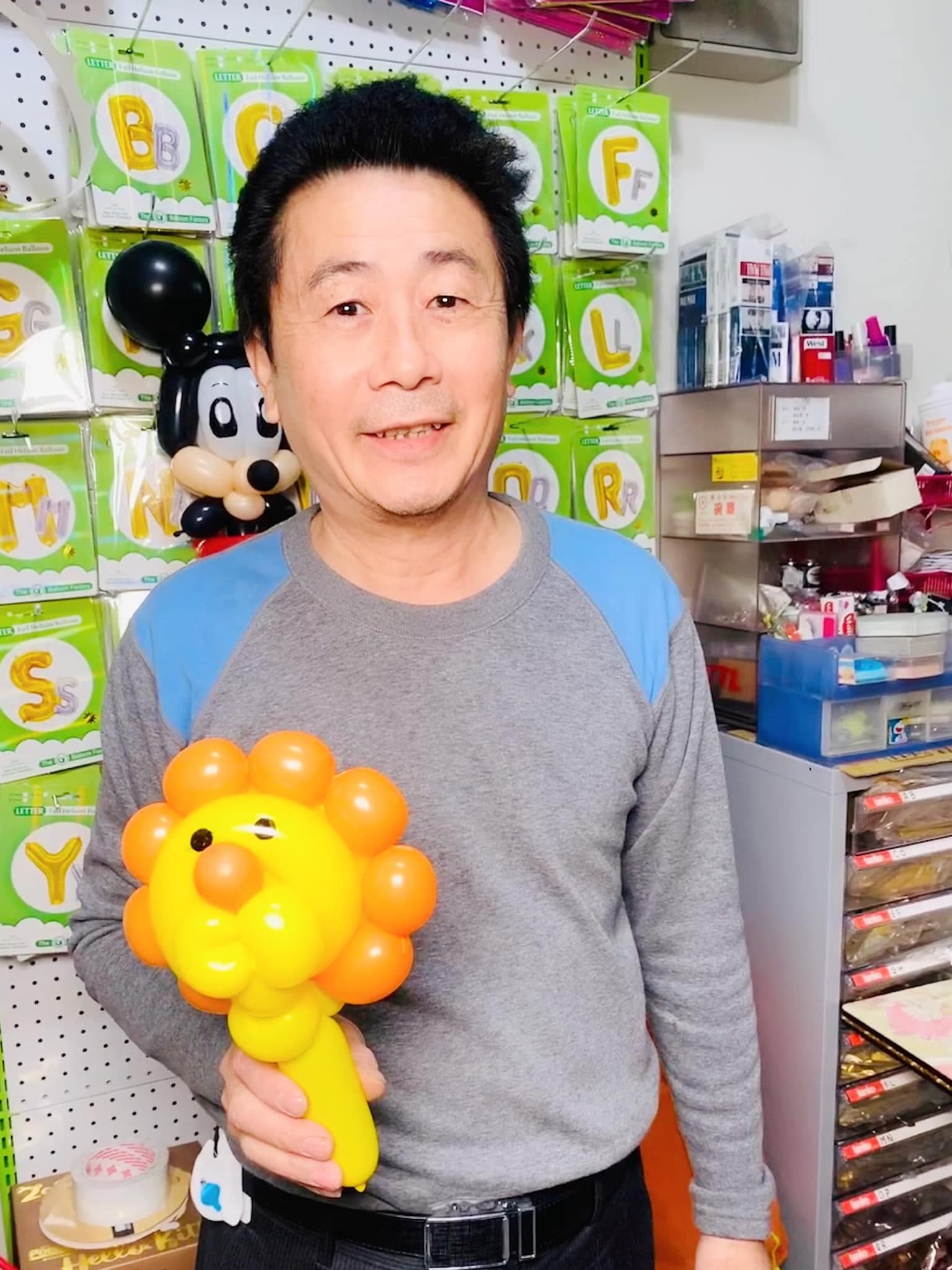 柯爹拿著黃色臉、橘色鬃毛的獅子造型手拿棒，背後掛著米奇