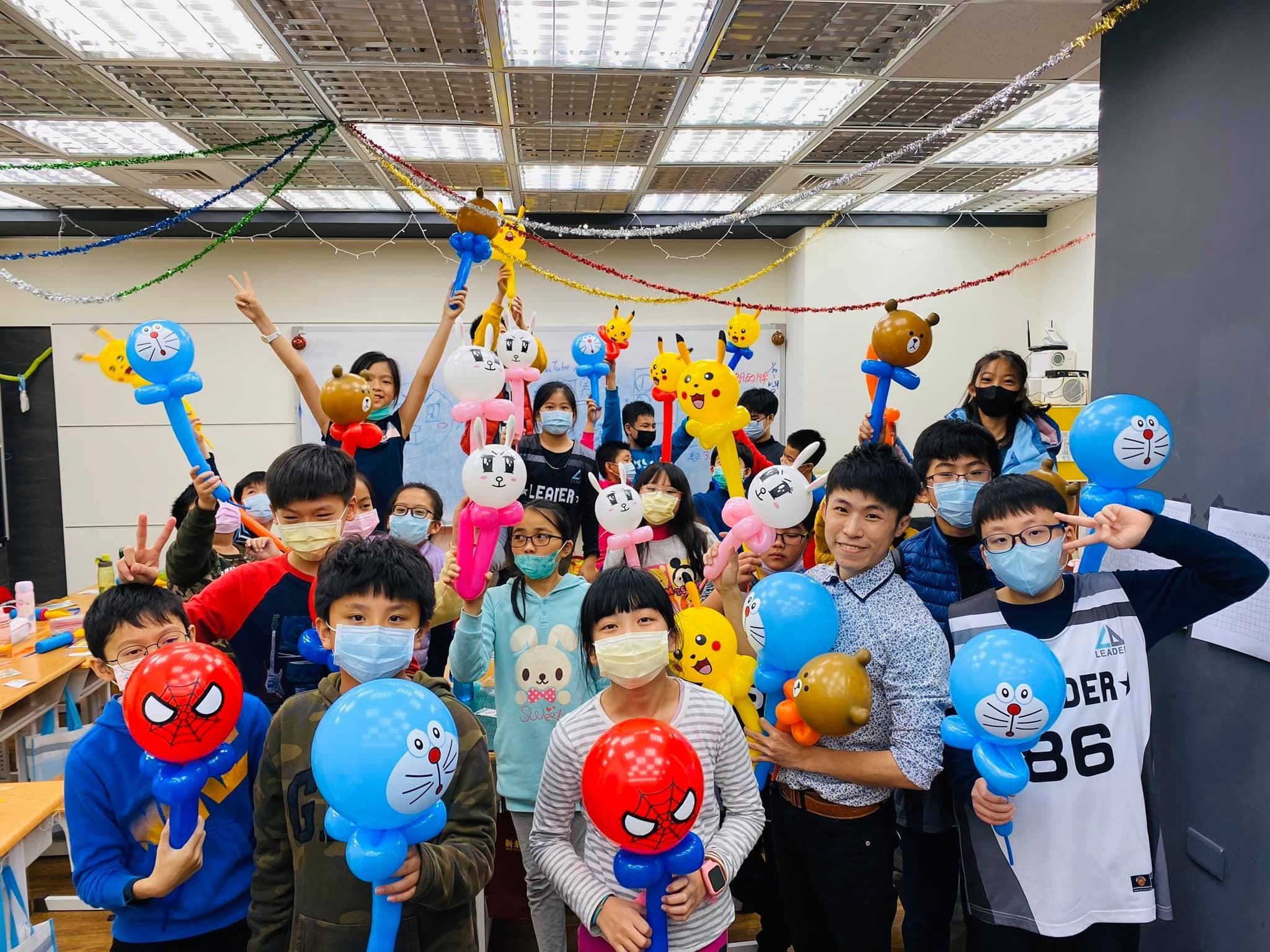 冬令營教室裡，戴口罩的學生舉著蜘蛛人、哆啦A夢與小熊造型氣球合照