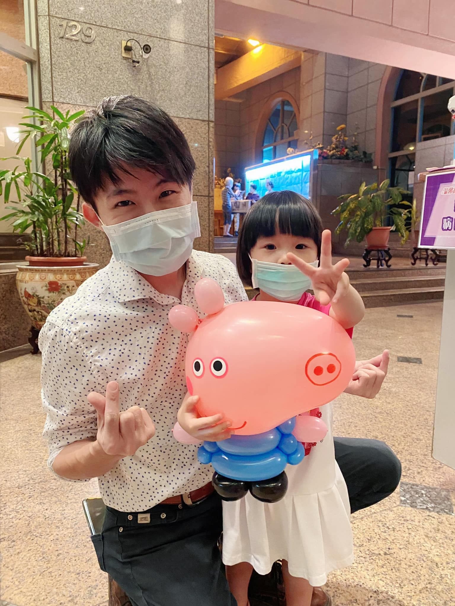 小女孩抱著穿藍色衣服的佩佩豬造型氣球，和我在大樓門口合照