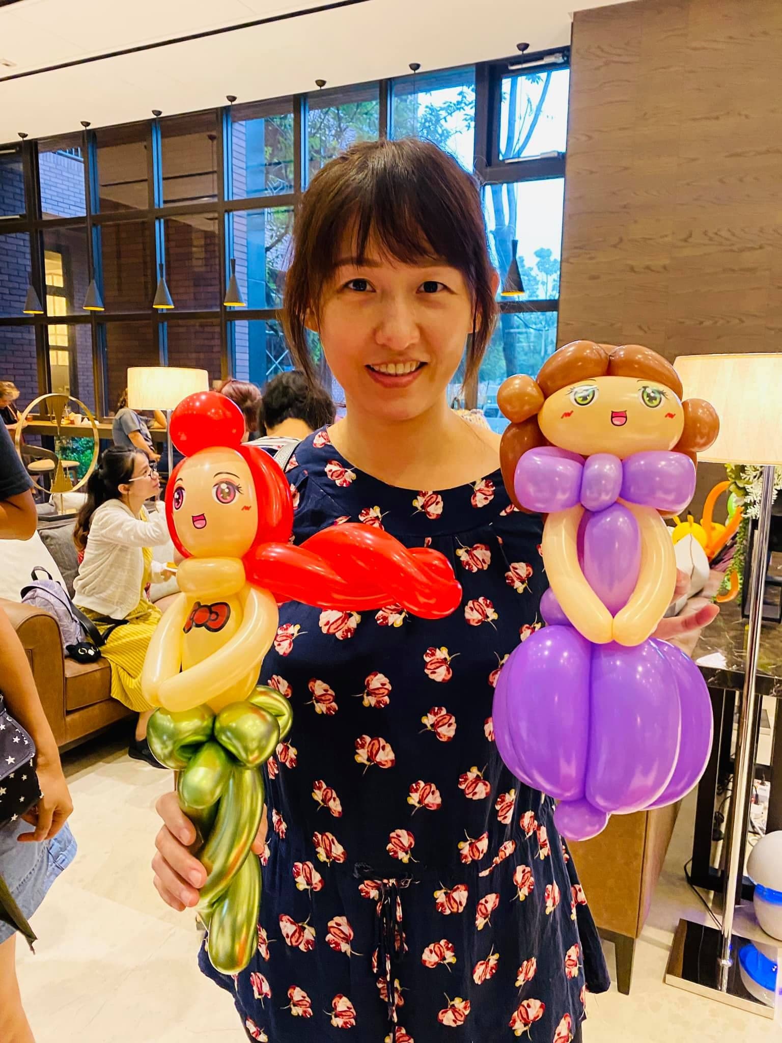 女士雙手各拿小美人魚與紫色蓬裙公主造型氣球