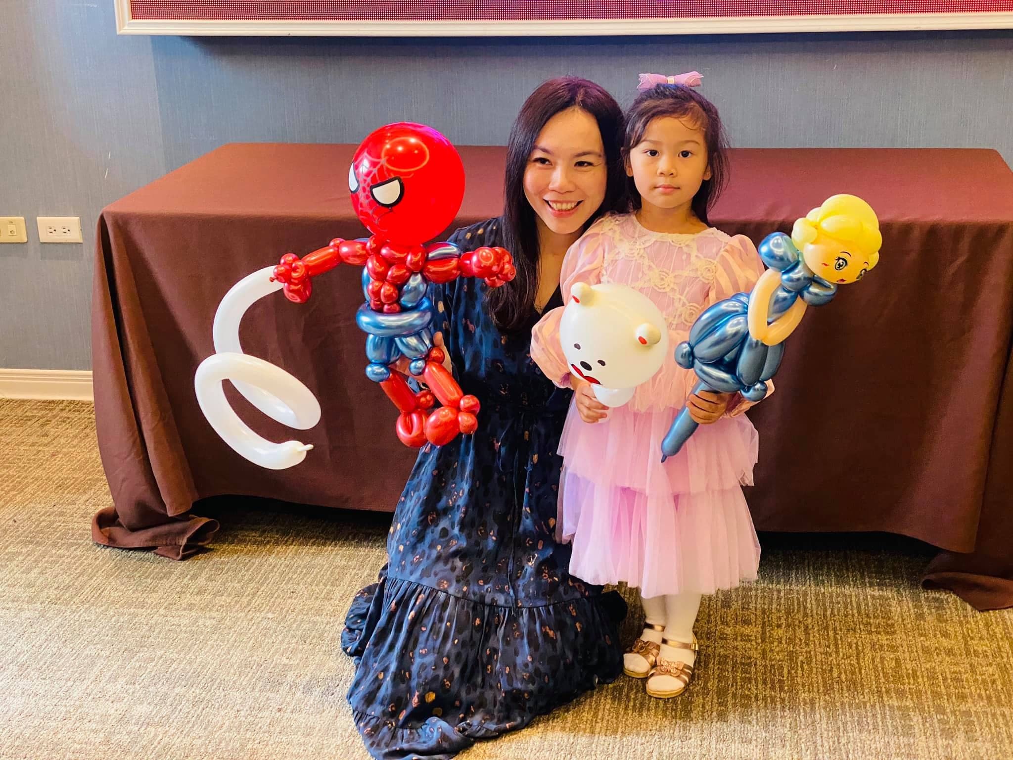 媽媽拿蜘蛛人氣球，女兒拿白熊與金髮藍裙公主氣球
