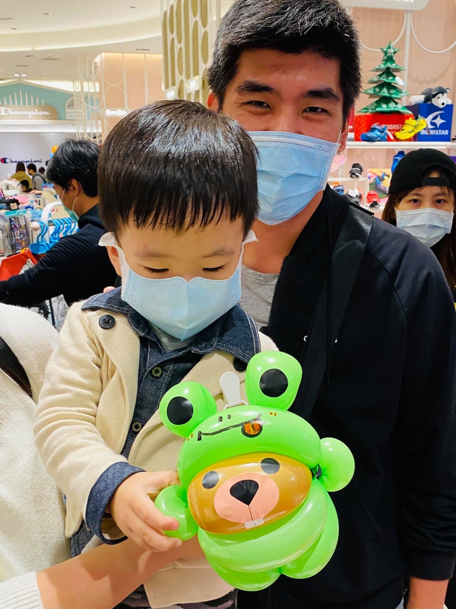 爸爸抱著小男孩，手上是綠色青蛙頭套海狸氣球
