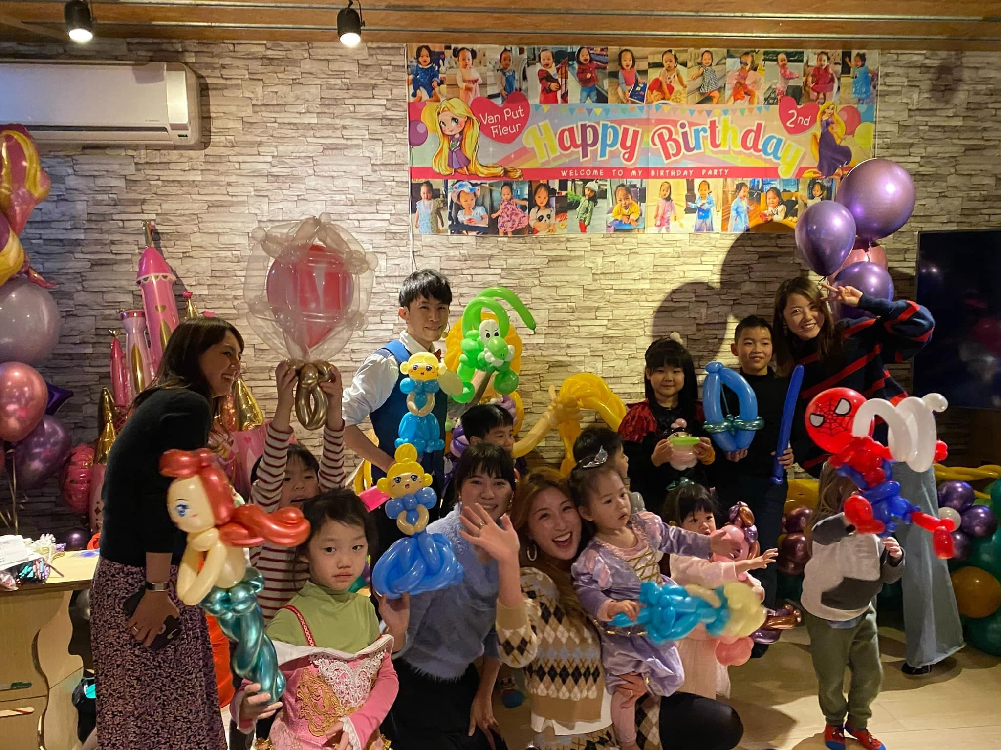 生日派對背板前大合照，大人小孩拿著小美人魚、蜘蛛人等氣球