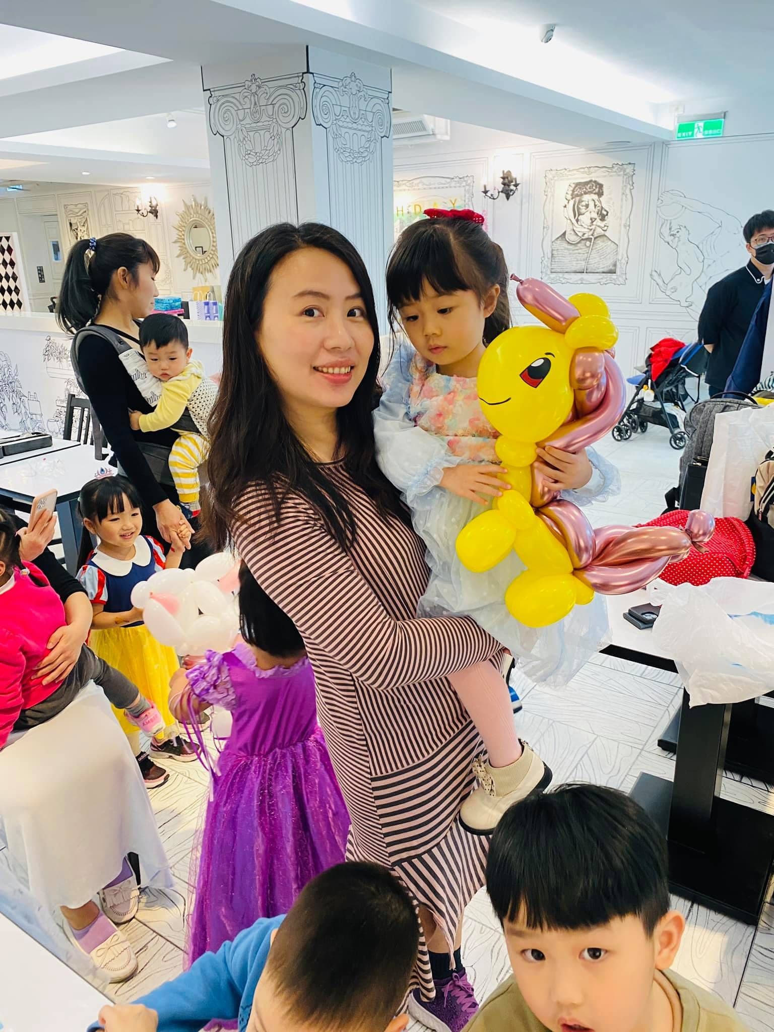 媽媽抱著女兒，女孩懷裡是粉紅鬃毛的黃色小馬氣球