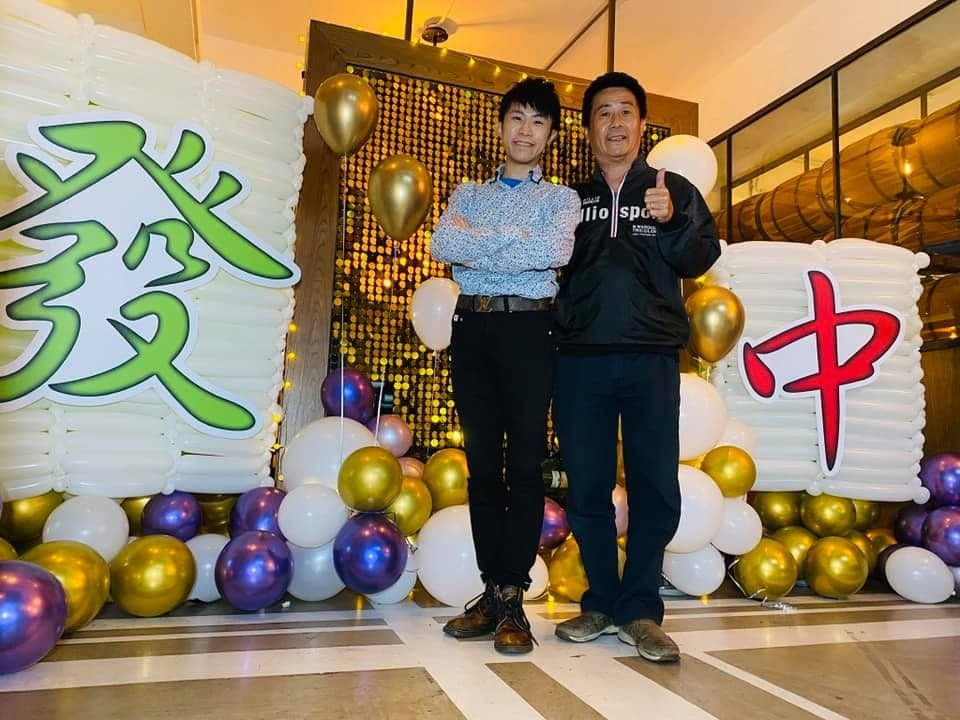 兩人站在發與中麻將牌氣球之間，背後是金色亮片牆