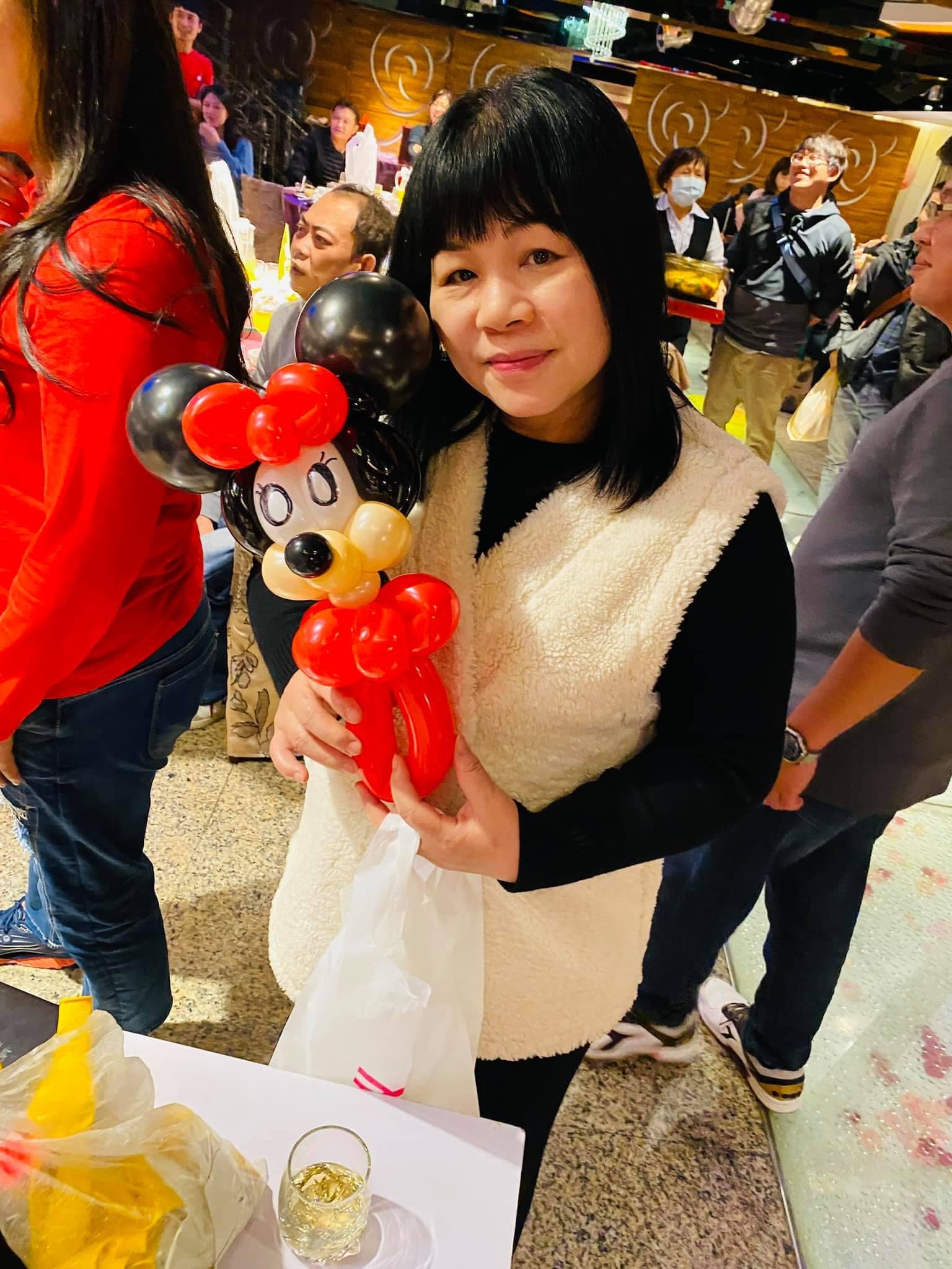 穿白色背心的女士抱著紅黑配色的米奇造型氣球