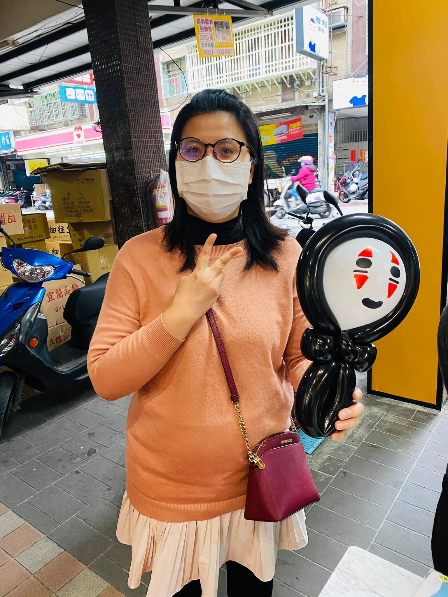 穿橘色毛衣的女士拿著無臉男氣球站在門市騎樓