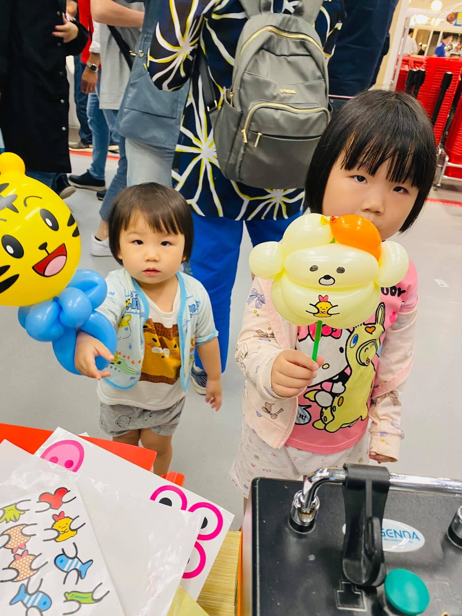 兩個小女孩拿著巧虎和布丁狗造型氣球站在攤位前
