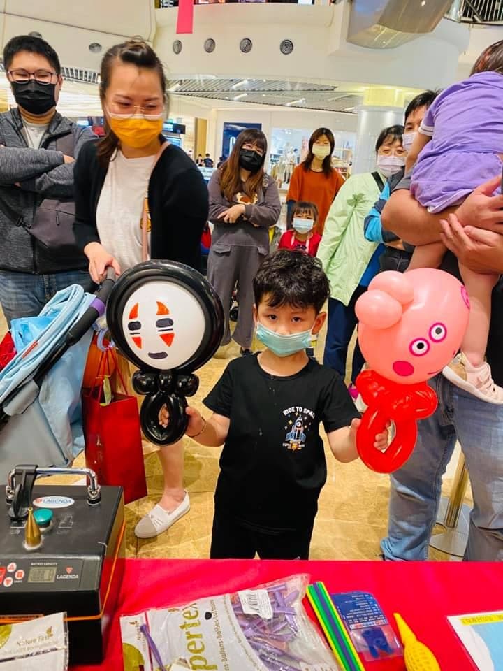 小男孩一手拿無臉男、一手拿佩佩豬造型氣球站在攤位前