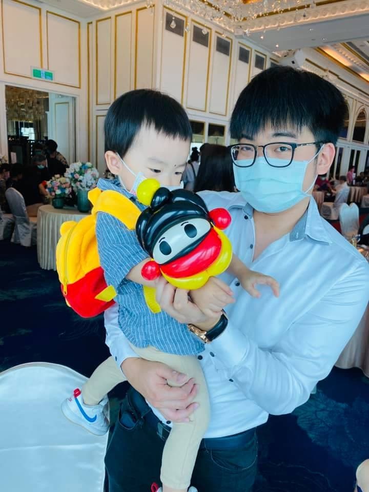 婚宴會場裡，男士抱著背著羅伊氣球的小男孩