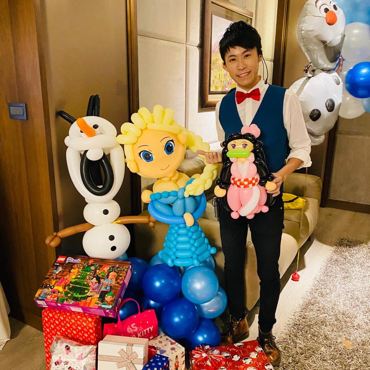 大型艾莎公主氣球站在藍色氣球底座上，左邊是雪寶氣球，我抱著禰豆子氣球站在右邊，前方堆滿禮物盒，牆上掛著雪寶鋁箔氣球