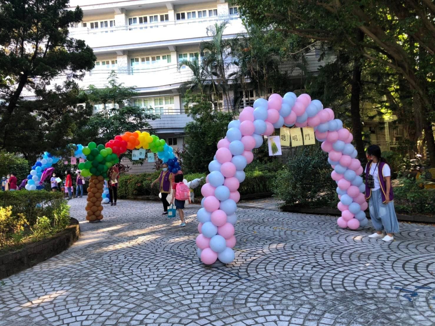 開學日校門口的粉藍拱門與彩虹樹拱門，學生背書包走進校園