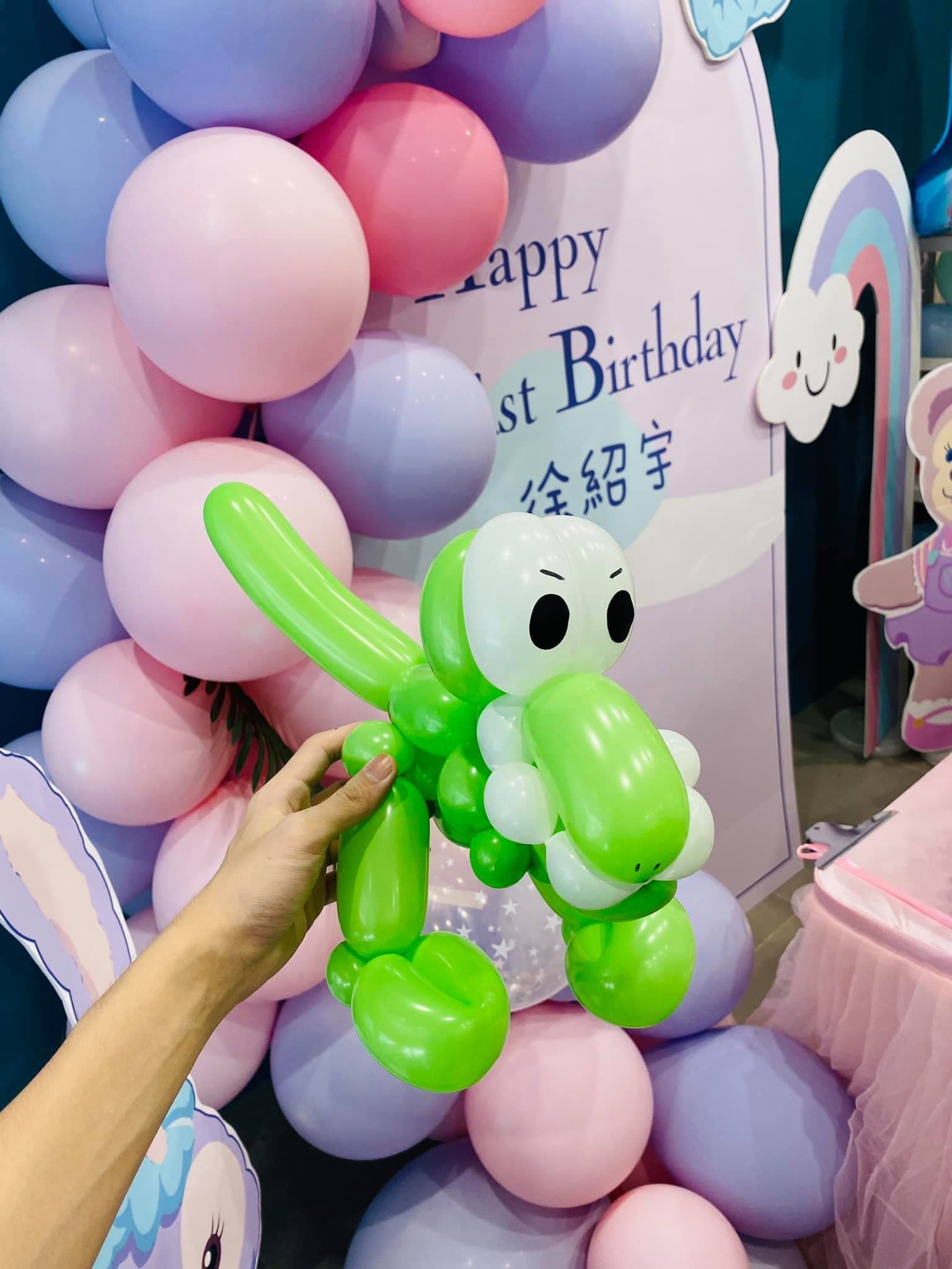 粉紫氣球背板前，手拿綠色恐龍造型氣球