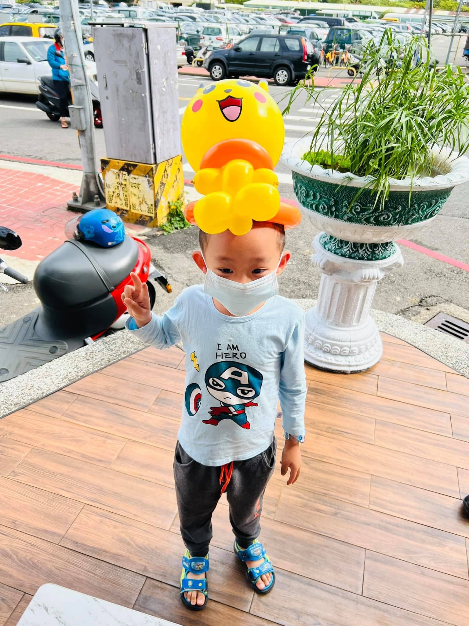 小男孩頭戴皮卡丘臉的黃色氣球帽，在門口比 YA