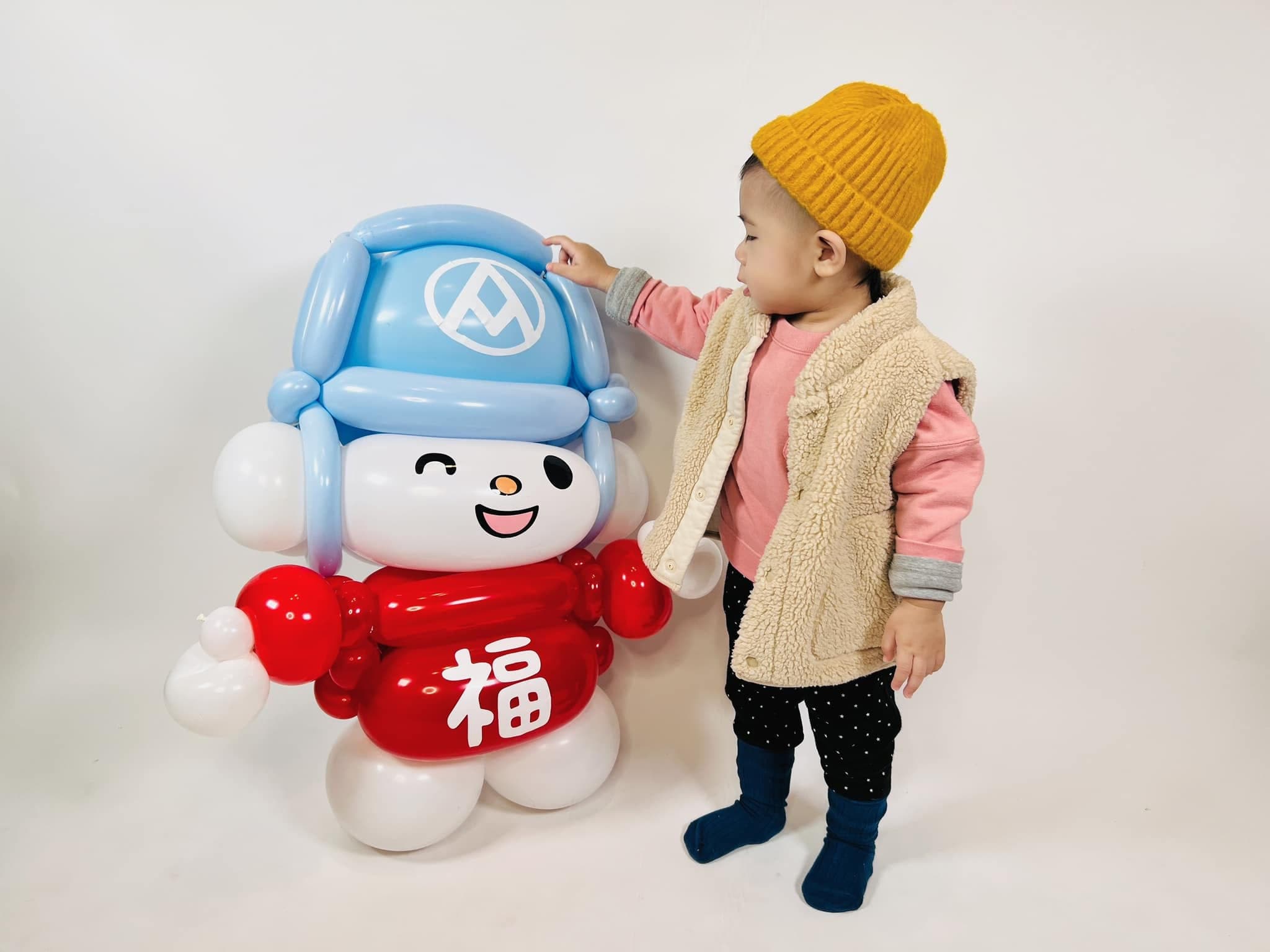 戴黃色毛帽的小小孩伸手摸福利熊氣球人偶的帽子