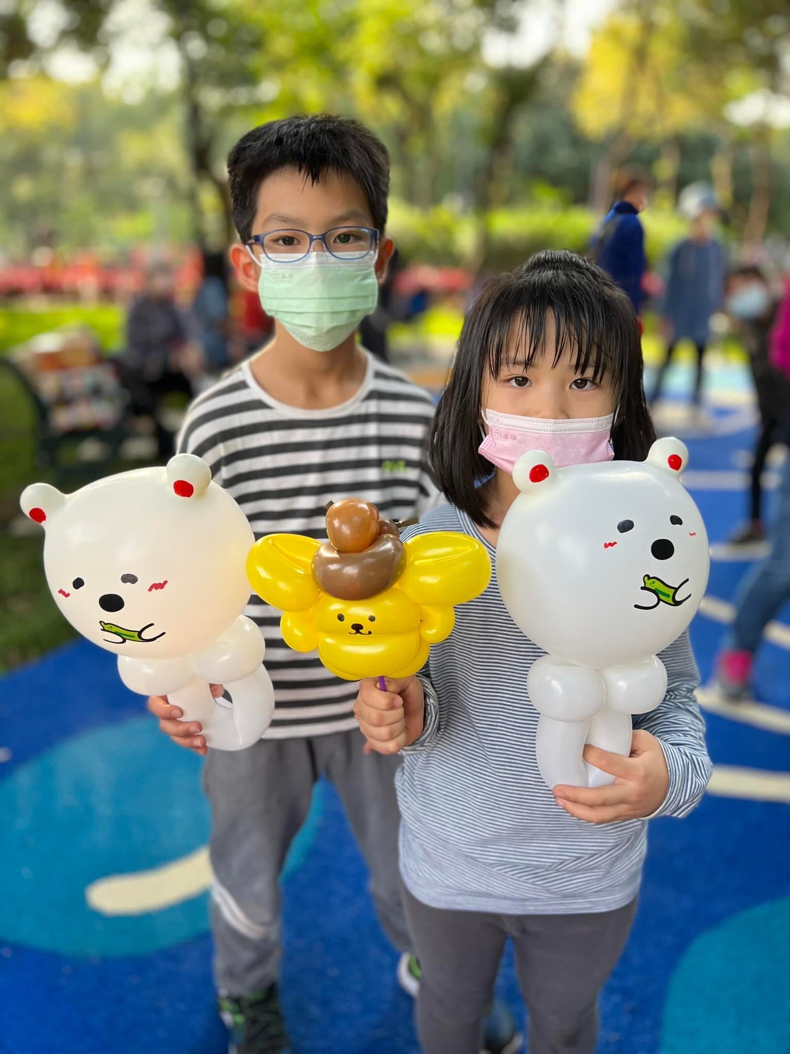 兩位小朋友拿著白色小熊與小蜜蜂造型氣球，板橋公園現場