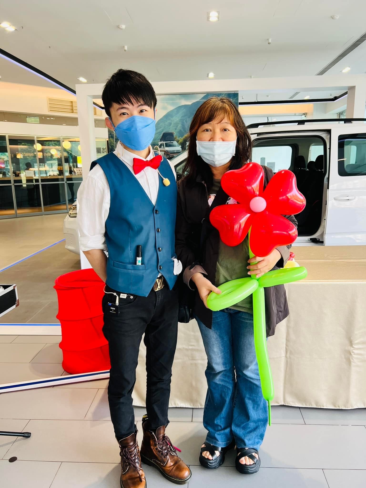 來賓拿著紅色大花造型氣球，在汽車展間與柯男合照