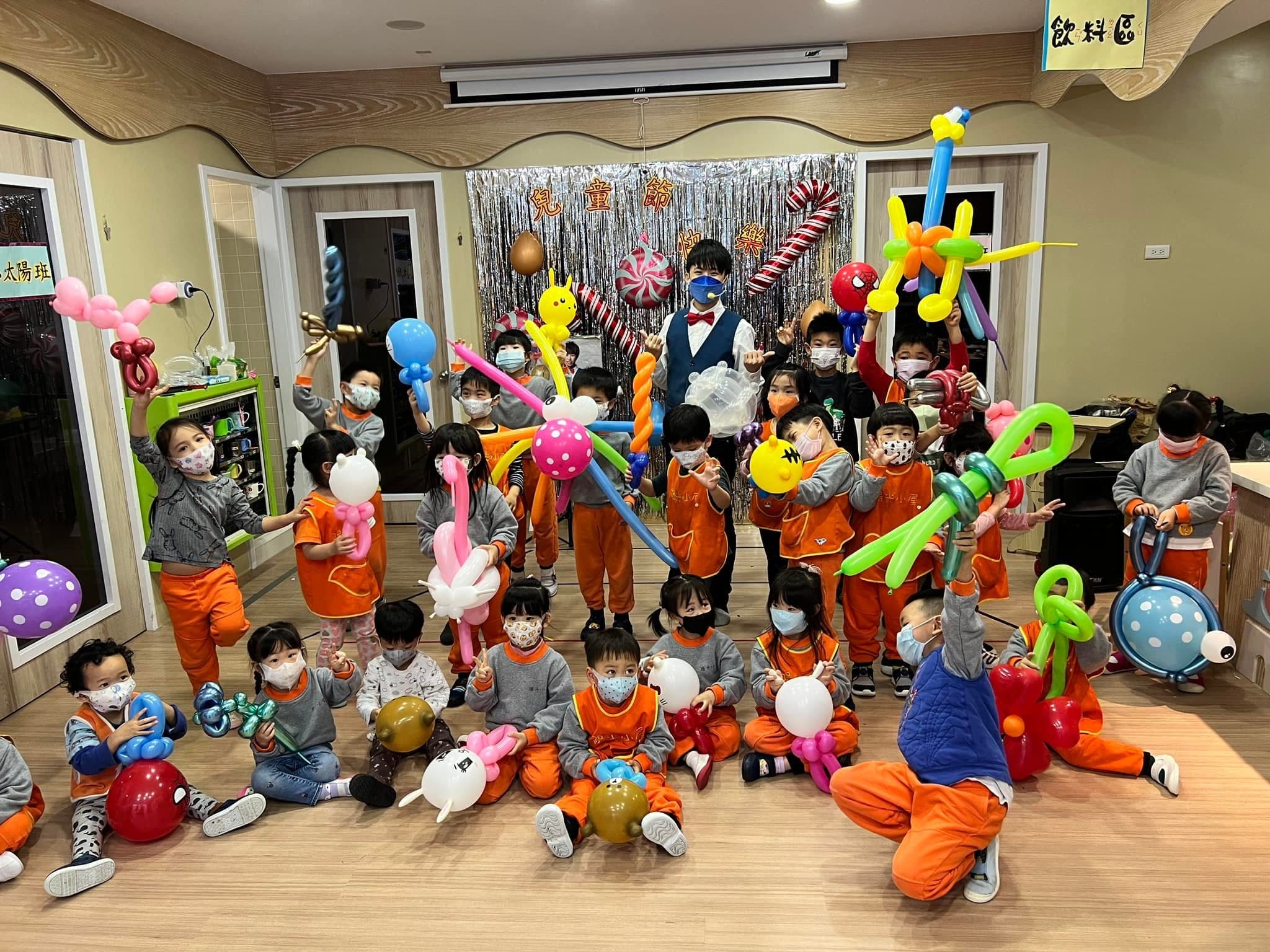 穿橘色園服的幼兒園小朋友舉著寶劍與花朵造型氣球