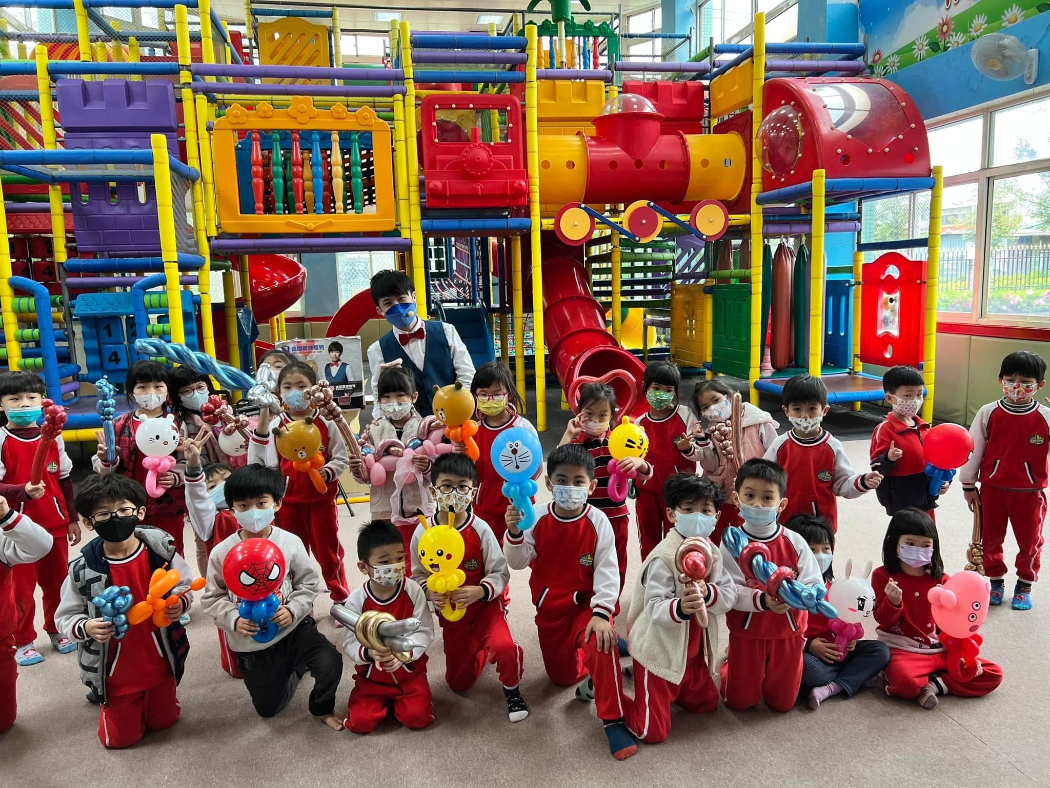 穿紅色園服的幼兒園小朋友在遊戲器材前拿造型氣球合照