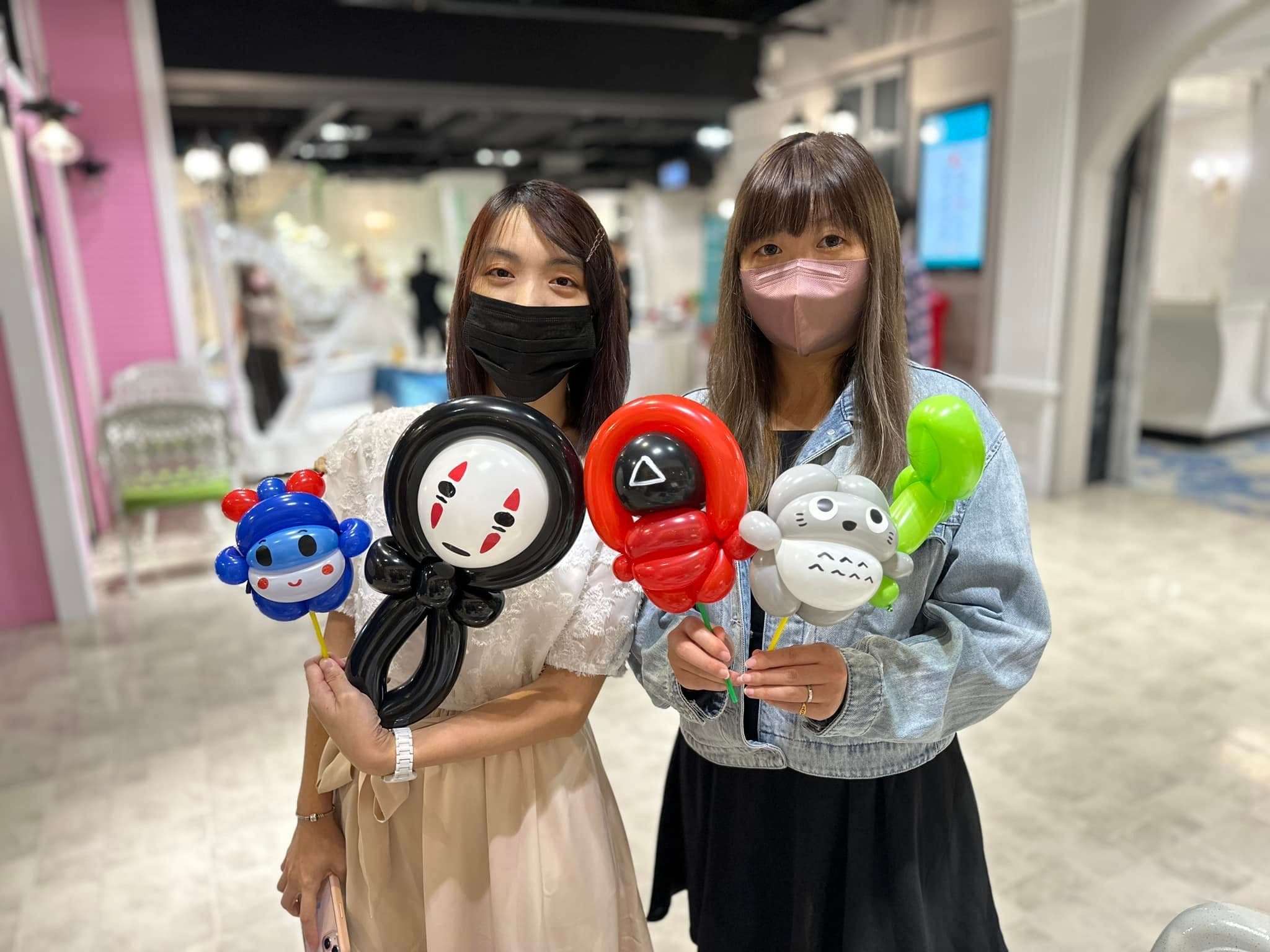 兩位女賓客並肩，手上是藍色小機器人、無臉男、魷魚遊戲面具與龍貓氣球