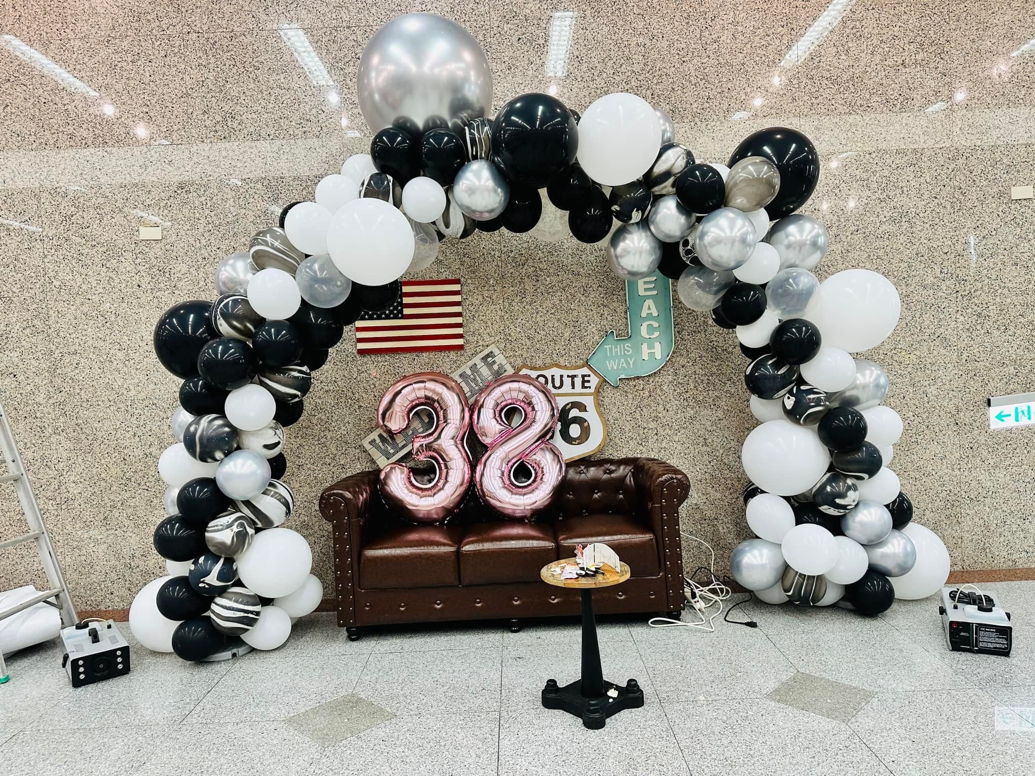 皮沙發上放著玫瑰粉色數字 38 氣球，背景有美國國旗與 Route 66 路牌