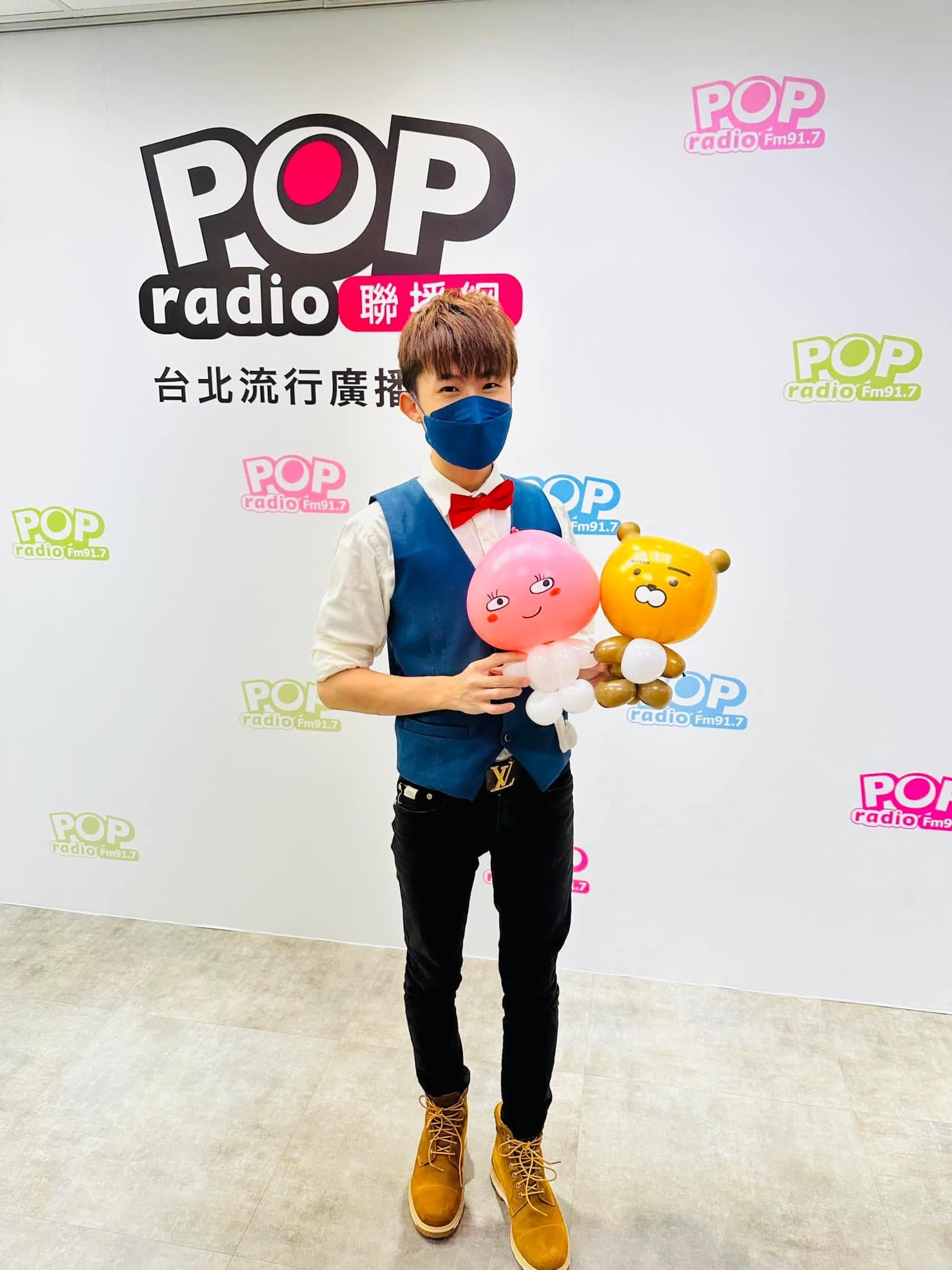 我在 POP Radio 背板前，手捧黃色小熊與粉紅桃子造型氣球