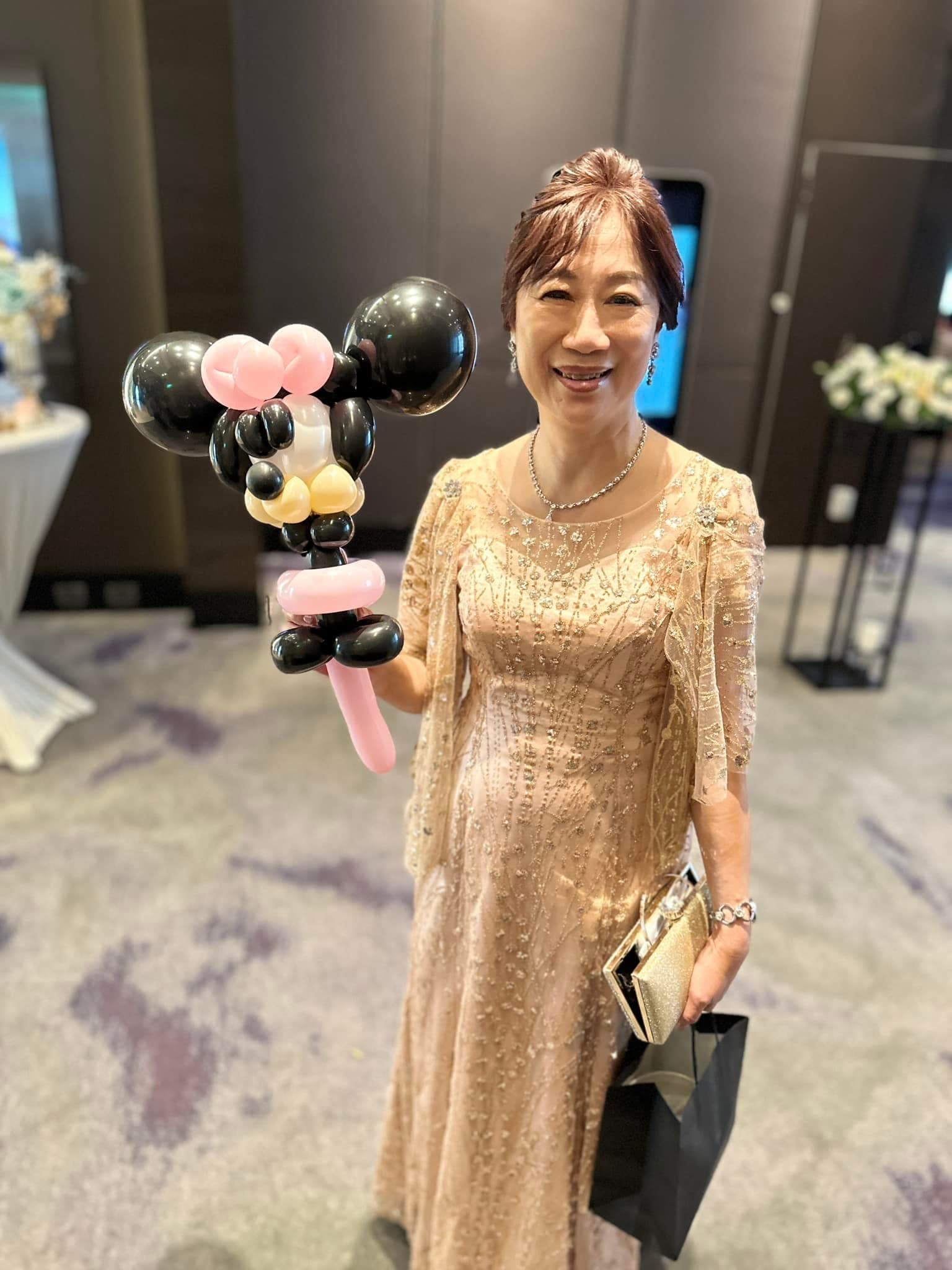 穿金色禮服的長輩拿著粉紅蝴蝶結的米妮造型氣球