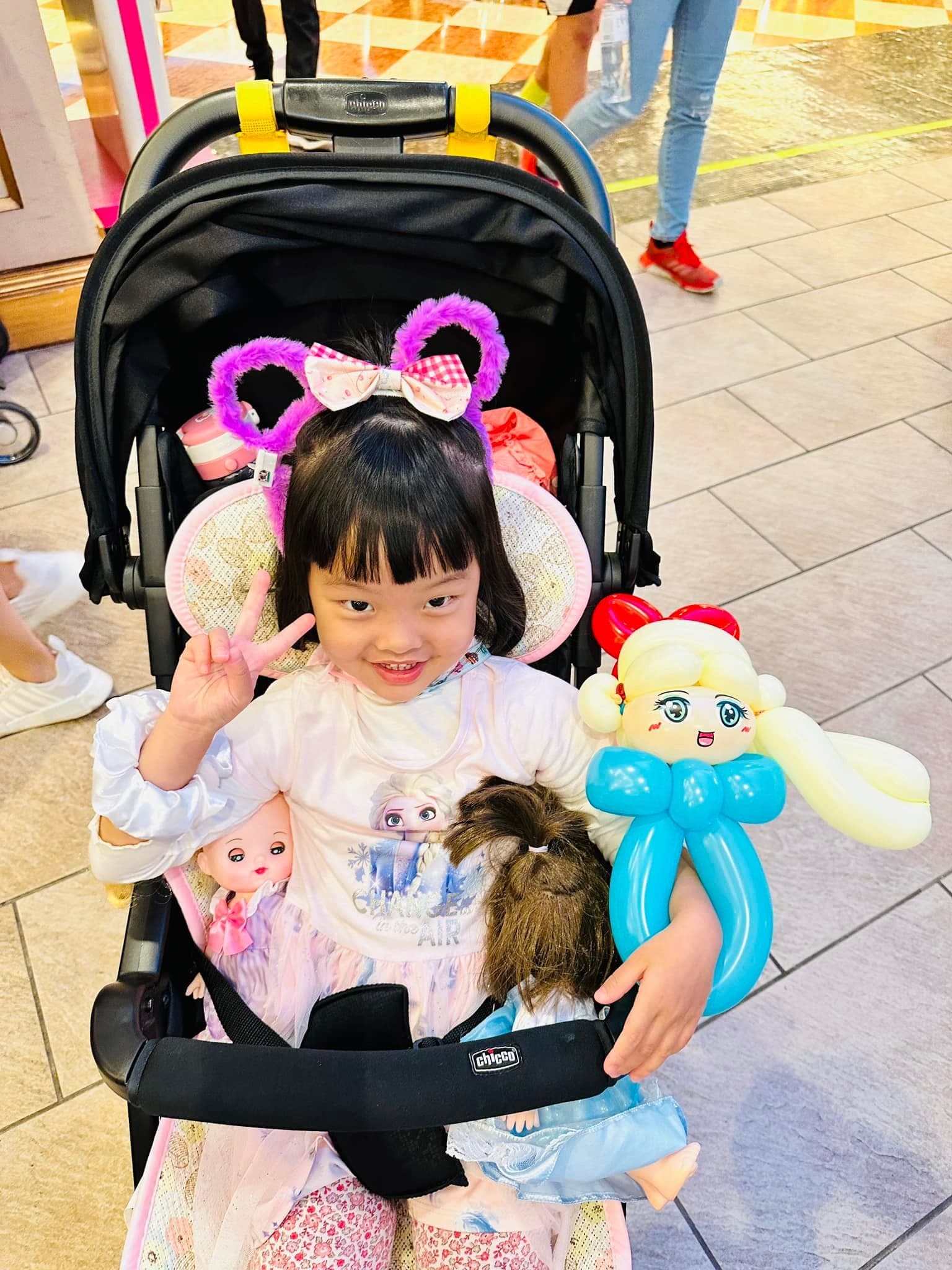 坐在推車裡的小女孩比 YA，懷裡抱著金色長辮、藍色禮服的艾莎氣球