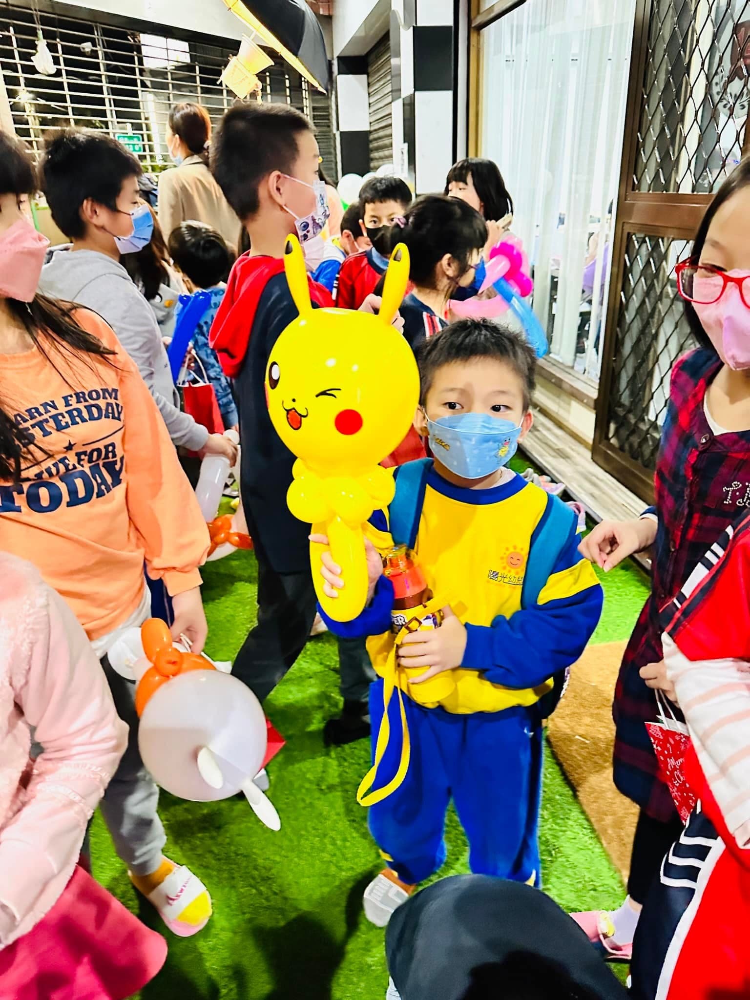 穿黃藍運動服的小男孩抱著眨眼的皮卡丘造型氣球