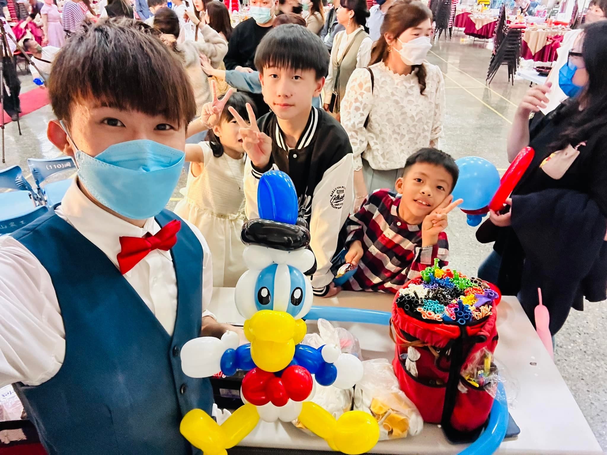 高雄婚禮會場，柯男自拍，桌上是唐老鴨造型氣球，身後孩子們比 YA