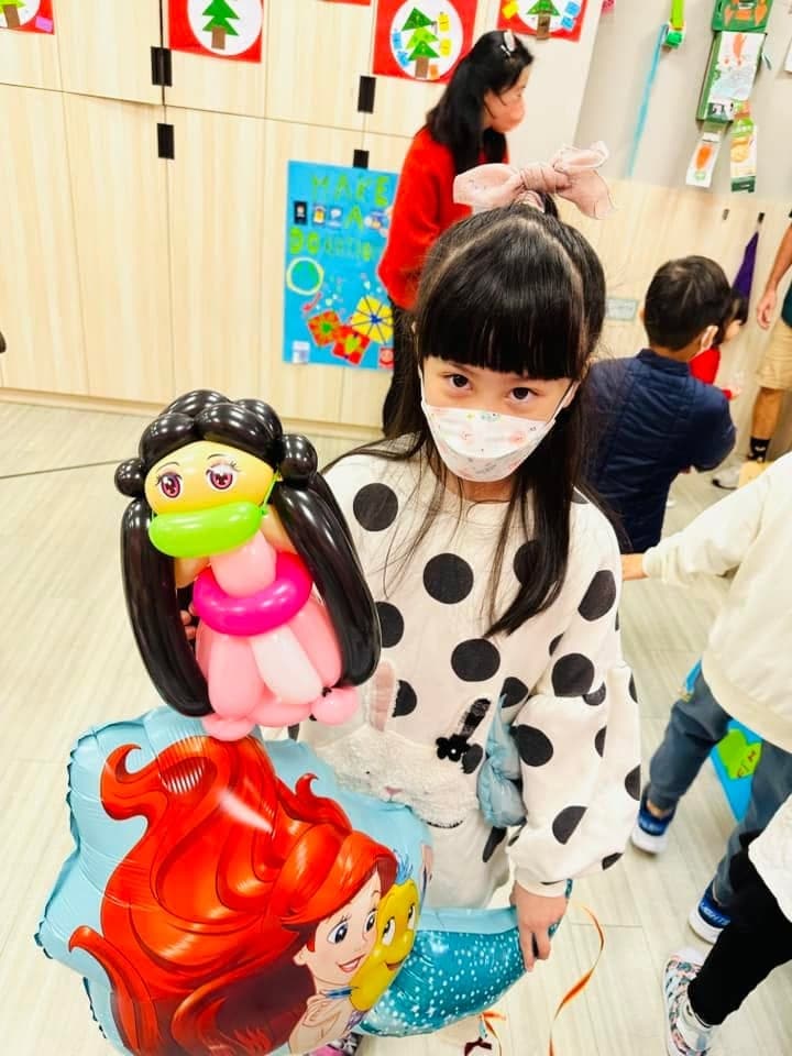 穿點點上衣的女孩拿著黑色長髮、戴綠色口罩的娃娃造型氣球