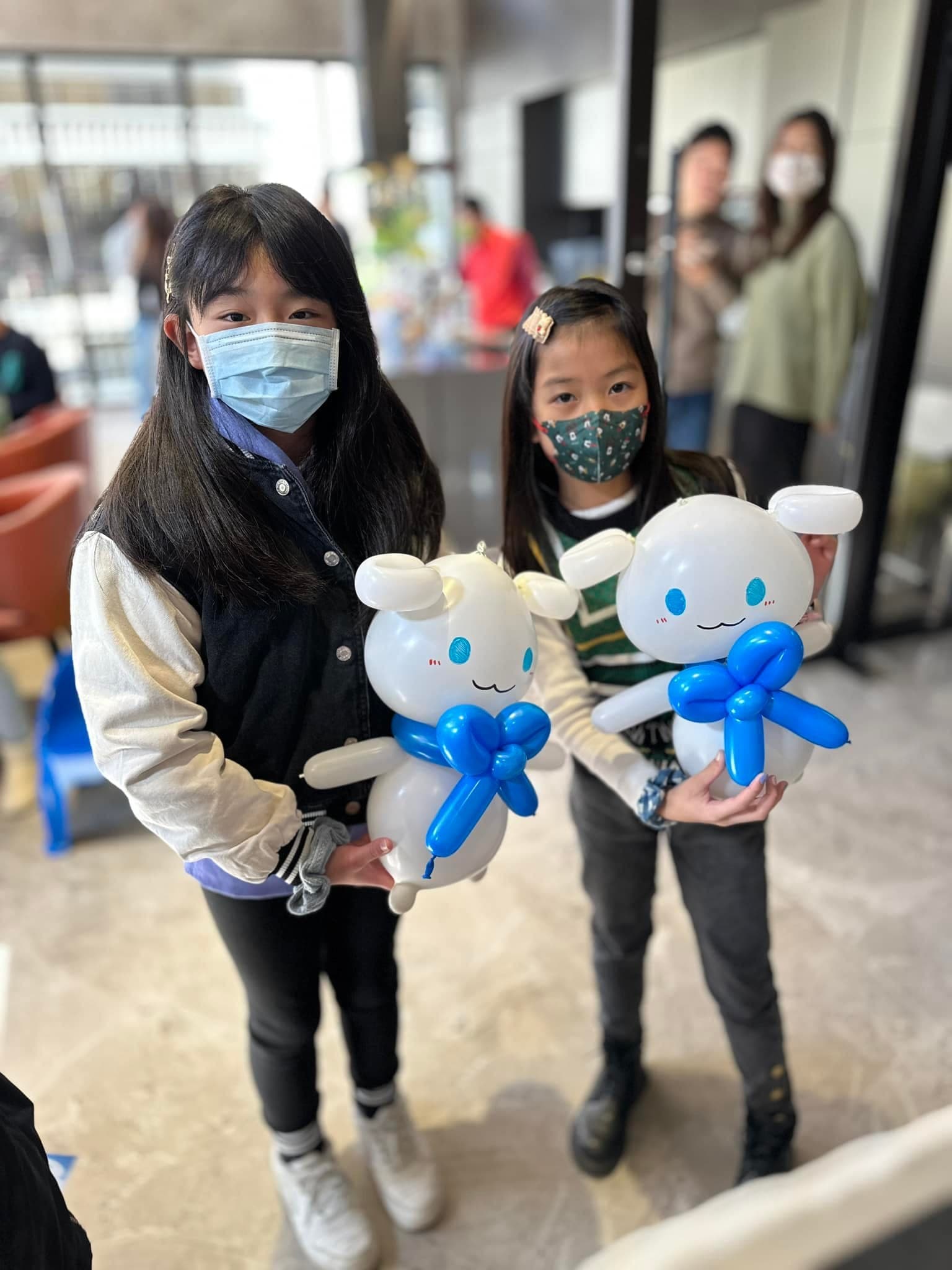 兩個女孩各抱一隻白色大耳朵、藍色蝴蝶結的大耳狗造型氣球